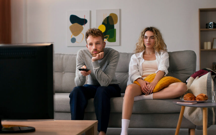 a couple sitting together on a couch and watching tv